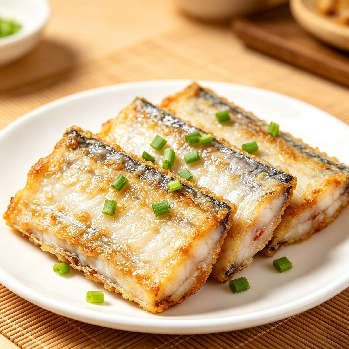 Pan-fried beltfish sections topped with spring onion on a white plate