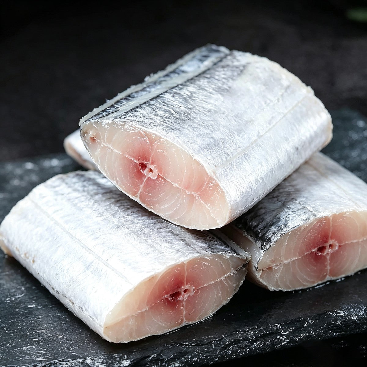 Close-up of pale silver beltfish steaks stacked on black slate